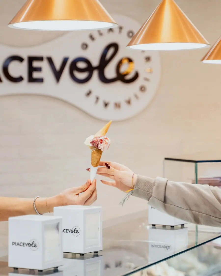 Cono gelato passato al banco di Gelateria Piacevole, con il logo sullo sfondo
